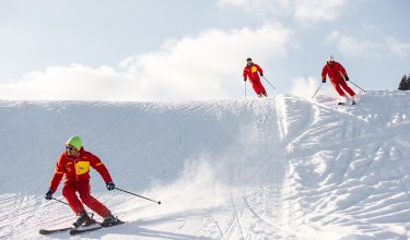 Drei Skilehrer in Rot fahren dynamisch eine verschneite Piste hinab