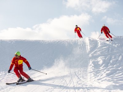 Drei Skilehrer in Rot fahren dynamisch eine verschneite Piste hinab