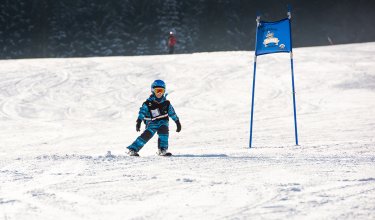 Kind im Skikurs fährt auf Piste neben blauem Torbogen