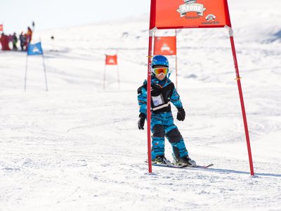 Kind im Skirennen fährt unter rotem Torbogen auf der Piste hindurch