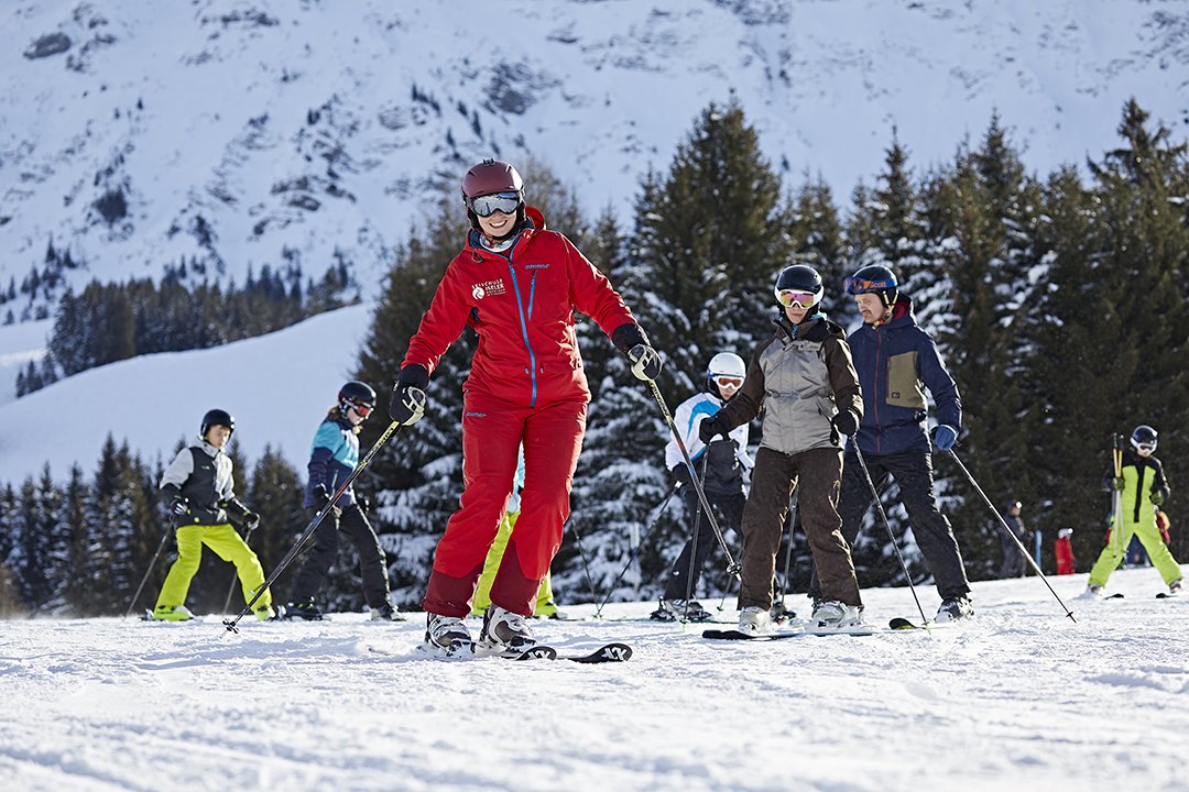 Skilehrerin führt Skigruppe über sonnige Piste mit Tannenwald