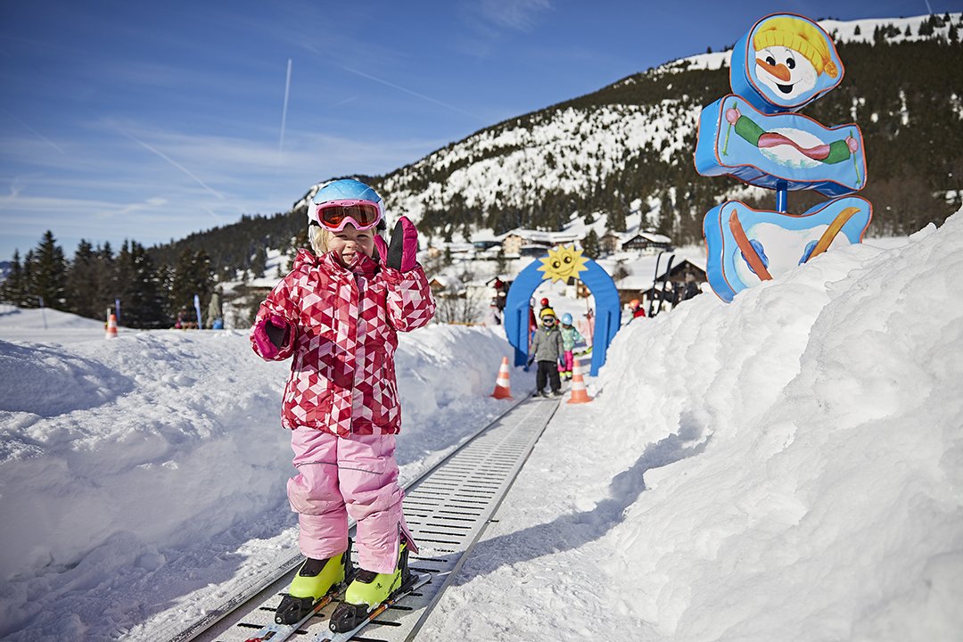 Kind auf Förderband im Skikindergarten mit bunter Deko