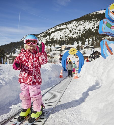 Kind auf Förderband im Skikindergarten mit bunter Deko