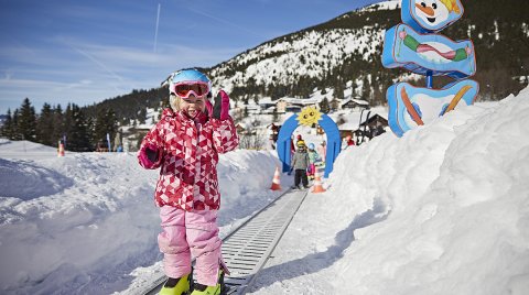 Kind auf Förderband im Skikindergarten mit bunter Deko