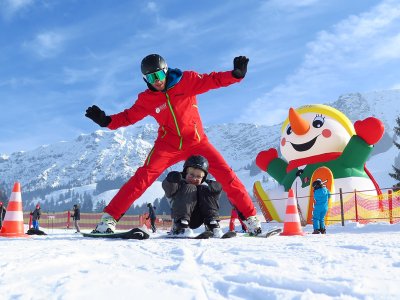 Skilehrer hilft Kind auf Schnee vor großem Schneemann