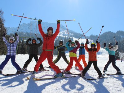 Skilehrerin mit Kindern hebt Skistöcke auf sonniger Piste