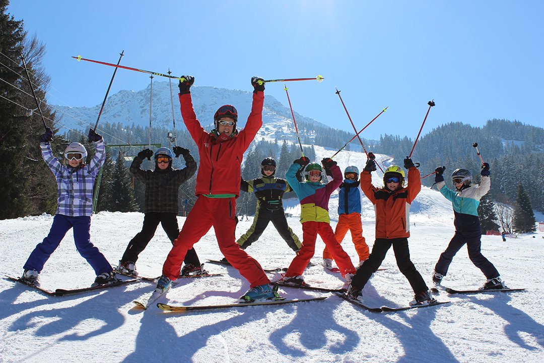 Skilehrerin mit Kindern hebt Skistöcke auf sonniger Piste