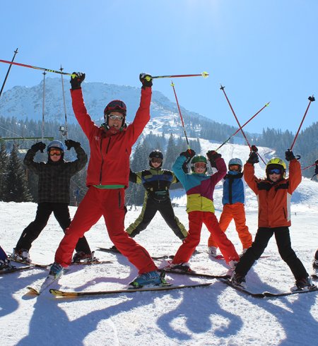Skilehrerin mit Kindern hebt Skistöcke auf sonniger Piste