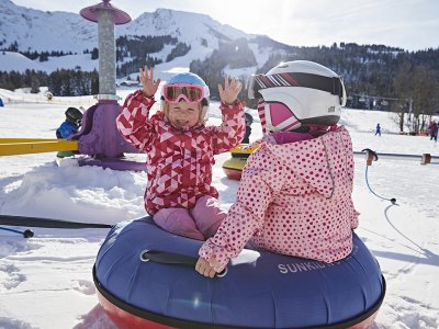 Zwei Kinder im Schnee beim Spielen auf einem blauen Reifenkarussell