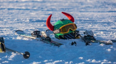 Skiausrüstung im Schnee mit Helm und roten Teufelshörnern