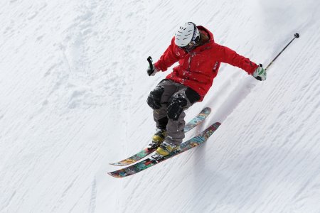 Skifahrer in roter Jacke springt über eine verschneite Piste