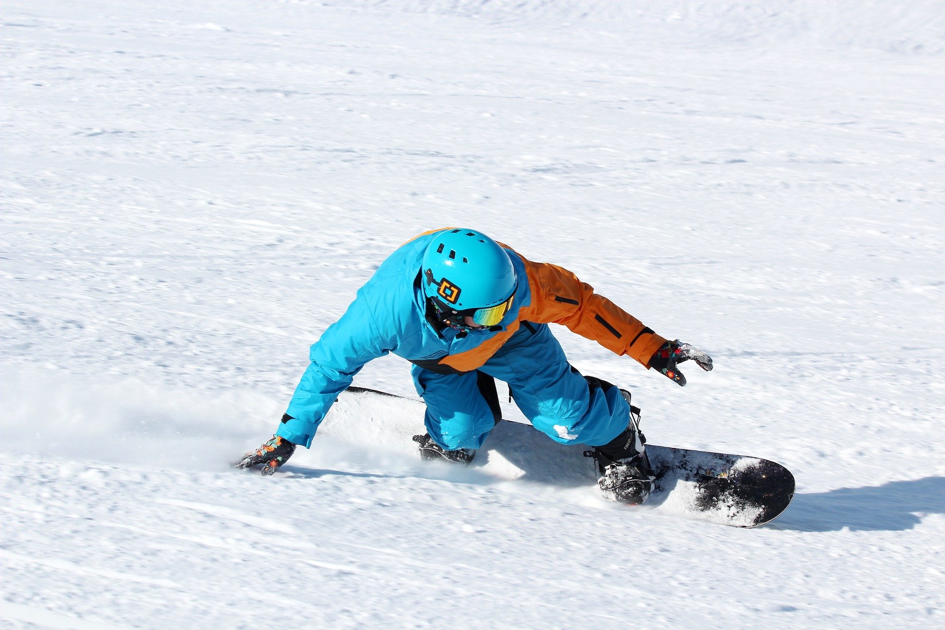 Snowboarder beim Carven auf der Piste in blau-oranger Kleidung