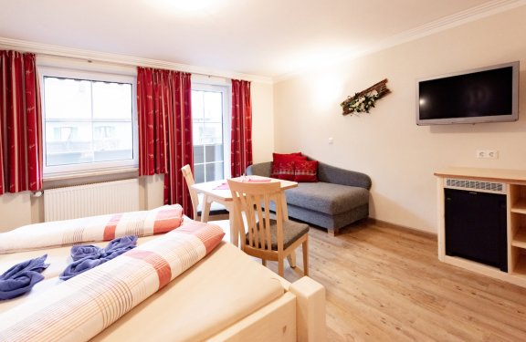 Zimmer mit Doppelbett, Tisch mit zwei Stühlen, TV und Balkon sowie Minibar.