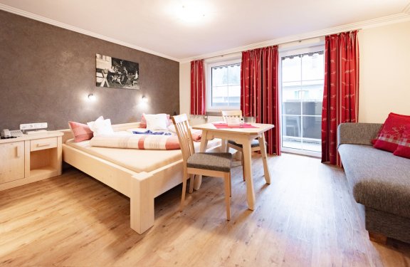 Zimmer mit Doppelbett, Tisch mit zwei Stühlen, Sofa und Balkon.