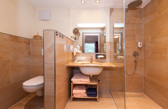Beige verfliestes Badezimmer mit WC, Waschbecken und ebenerdiger Dusche mit Glaswand.