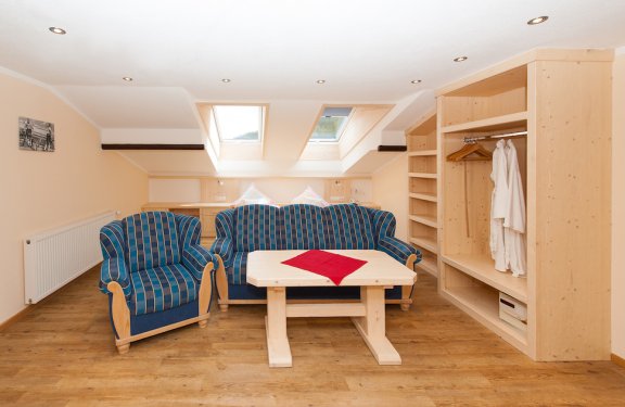 Doppelzimmer mit zwei Dachfenstern, blauem Sofa, Couchtisch und Kasten.