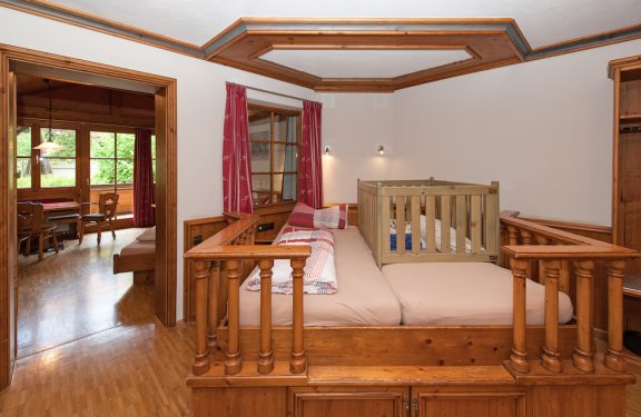 Doppelbett auf einem Holzpodest mit Holzpfeilern rundherum und Babybettaufsatz darauf.