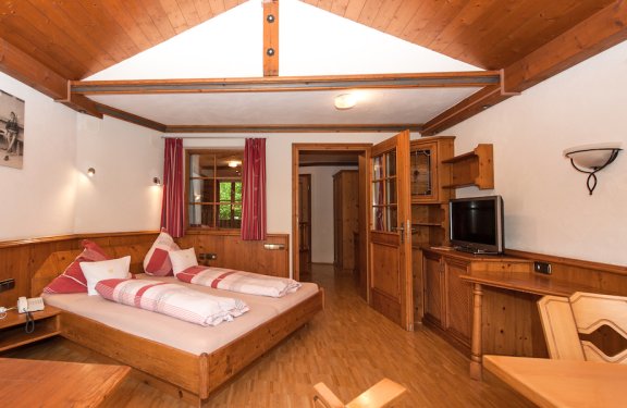 Helles Doppelzimmer mit vielen Holzvertäfelungen an den Wänden und Sitzecke.