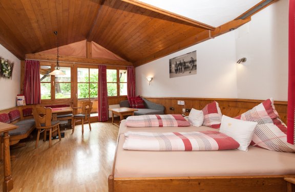 Helles Doppelzimmer mit vielen Holzvertäfelungen an den Wänden, gemütlicher Sitzecke und Balkon.