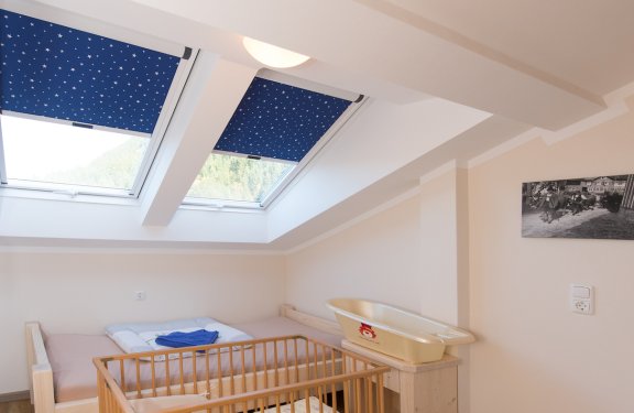 Helles Kinderzimmer mit keinem Bett, Gitterbett und zwei Dachfenstern.