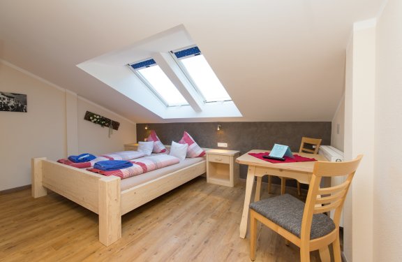 Doppelzimmer mit Tisch mit Stühlen und zwei Dachfenstern.