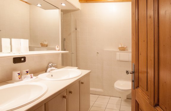 Bad mit weißen Fliesen, zwei Waschbecken, WC und Dusche.
