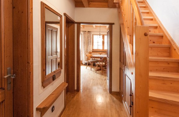 Eingangsbereich des Appartements mit Holzstiege nach oben und Küche im hinteren Bereich,
