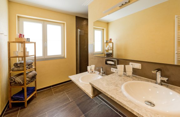 Badezimmer mit gelber Wandfarbe und dunklen Bodenfliesen und zwei Waschbecken.