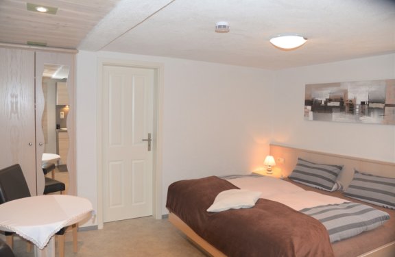 Helles Zimmer mit Doppelbett, Tisch und Sesseln.