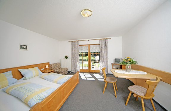Helles Zimmer mit Doppelbett, Tisch, Stühlen und Fernseher.