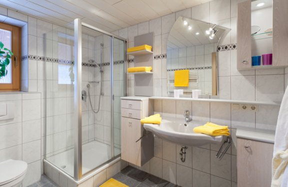 Badezimmer mit weißen Fliesen mit Eckdusche, Waschbecken und WC.
