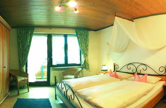 Helles Zimmer mit Doppelbett, Schrank, Stühlen und Balkon.