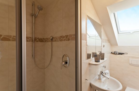 Badezimmer mit beigen Fliesen, Dusche und Waschbecken.