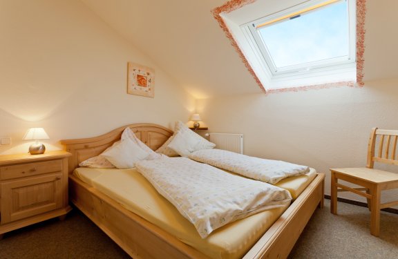 Aufgebettetes Doppelbett mit Nachtkästchen, Stuhl und Deckenfenster.
